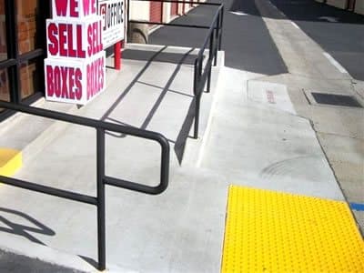 New concrete ADA ramp with yellow detectable warning surface and handrail