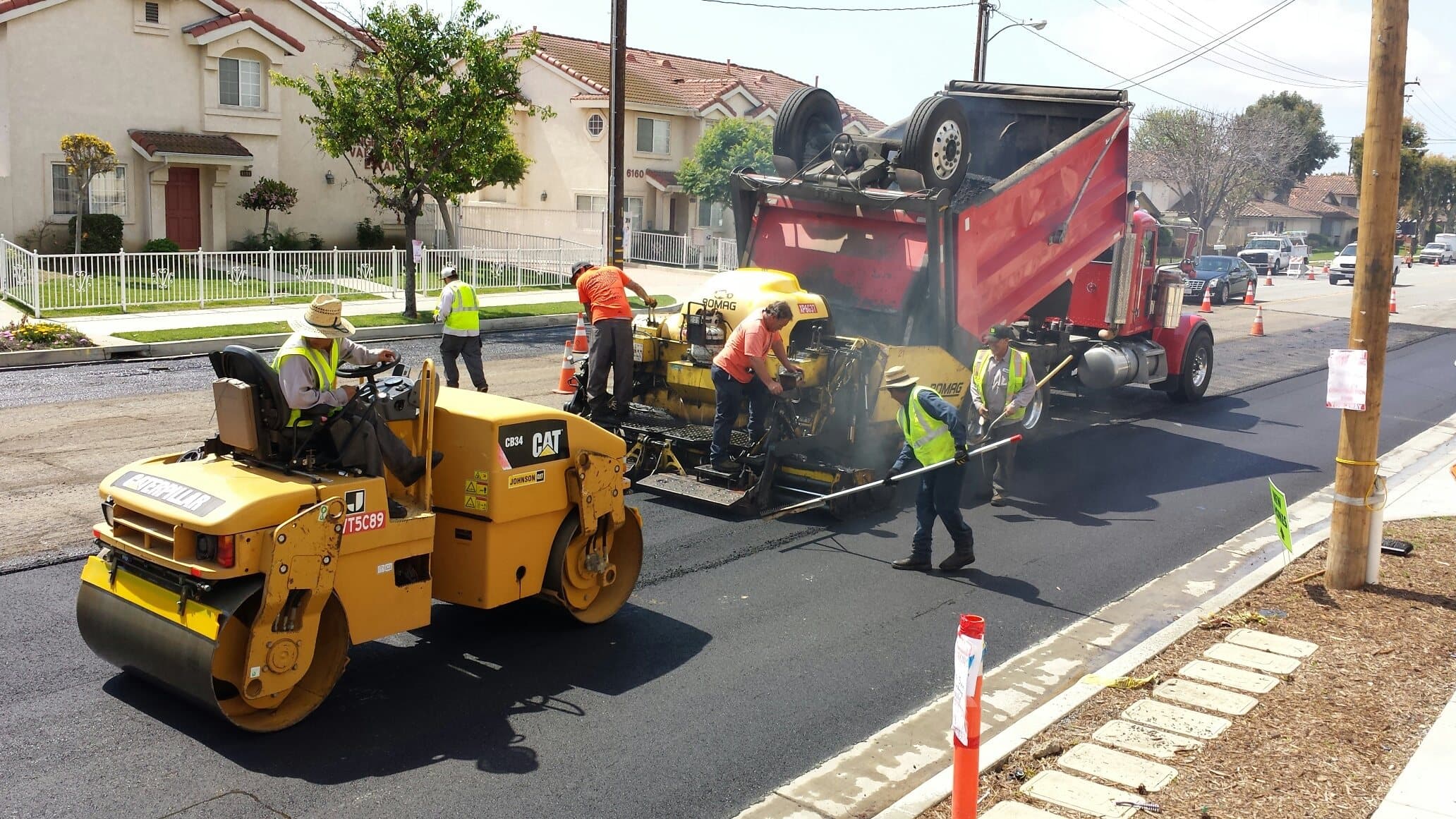 Paving crew, roller and dump truck working together on a street in Cypress