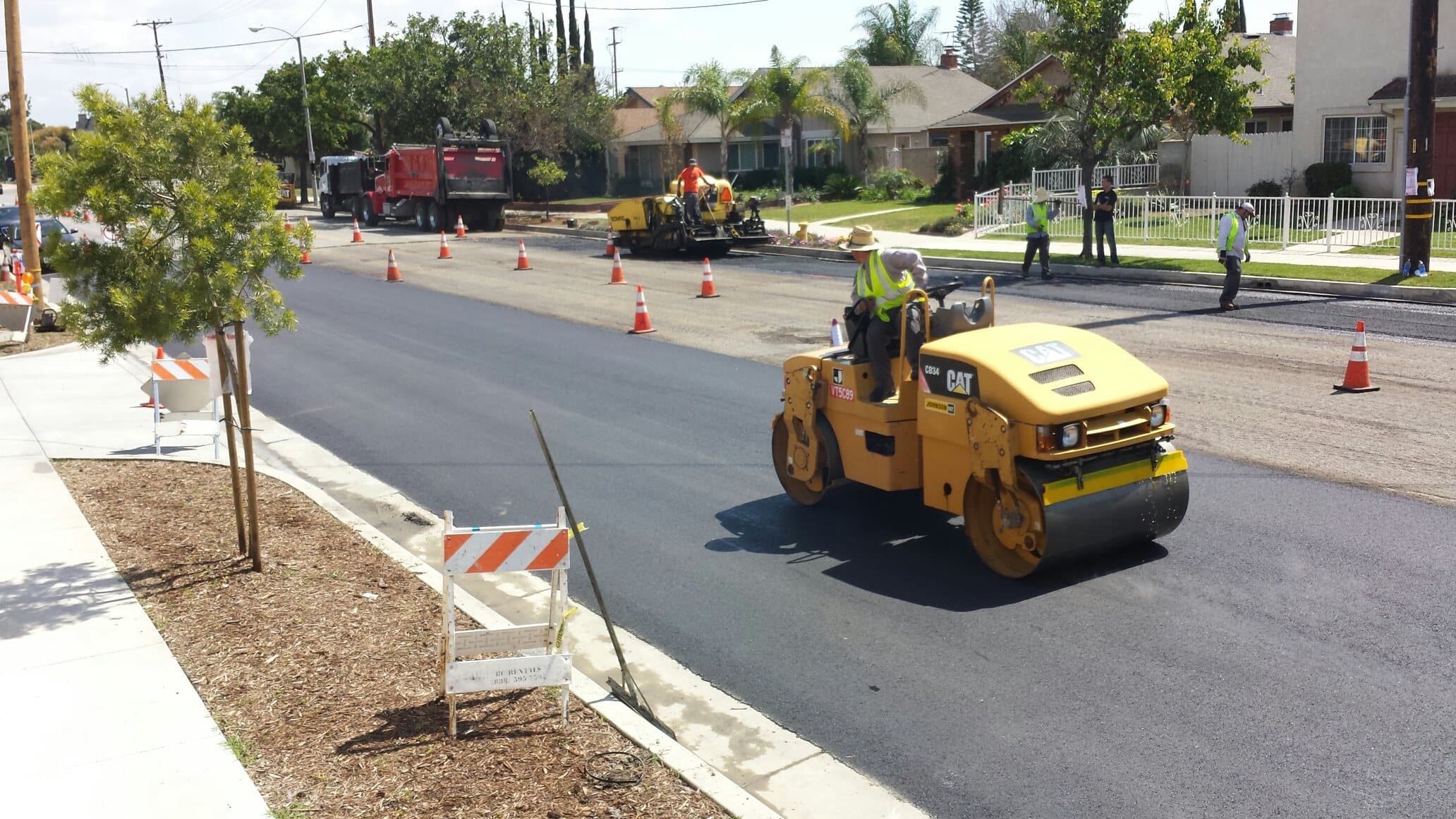 Roller compacting a new asphalt street in Cypress behind traffic control barricades