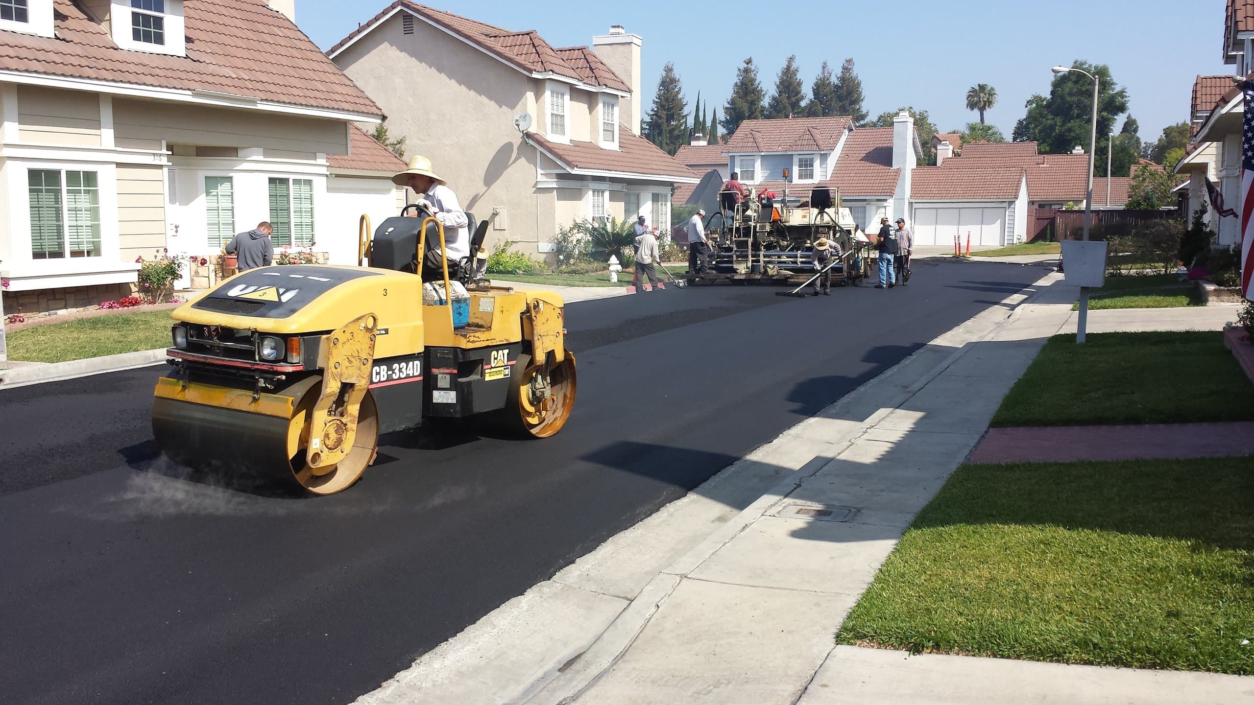 Roller finishing new asphalt along a residential curb and gutter
