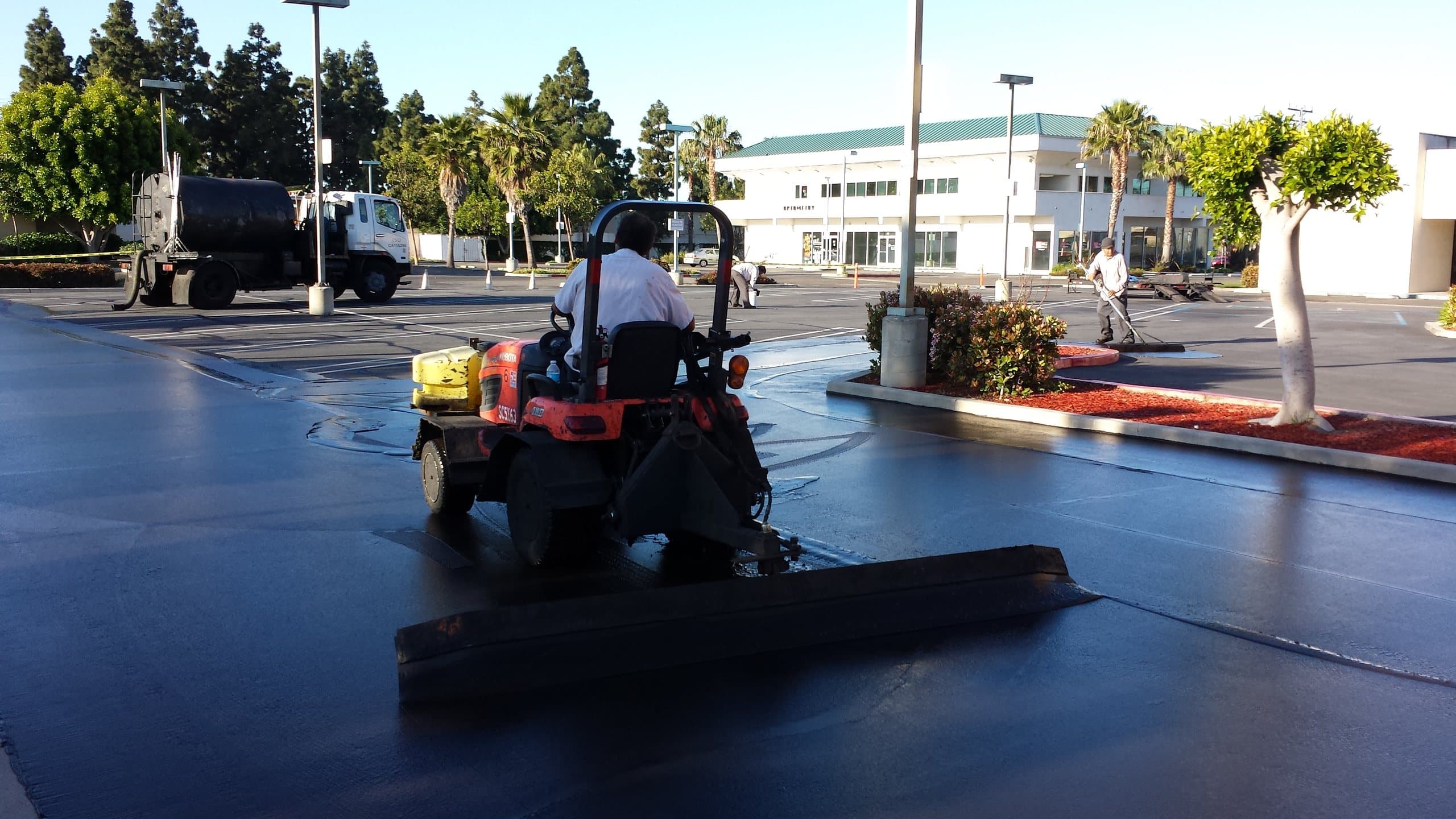 Ride-on squeegee machine spreading seal coat across a commercial parking lot