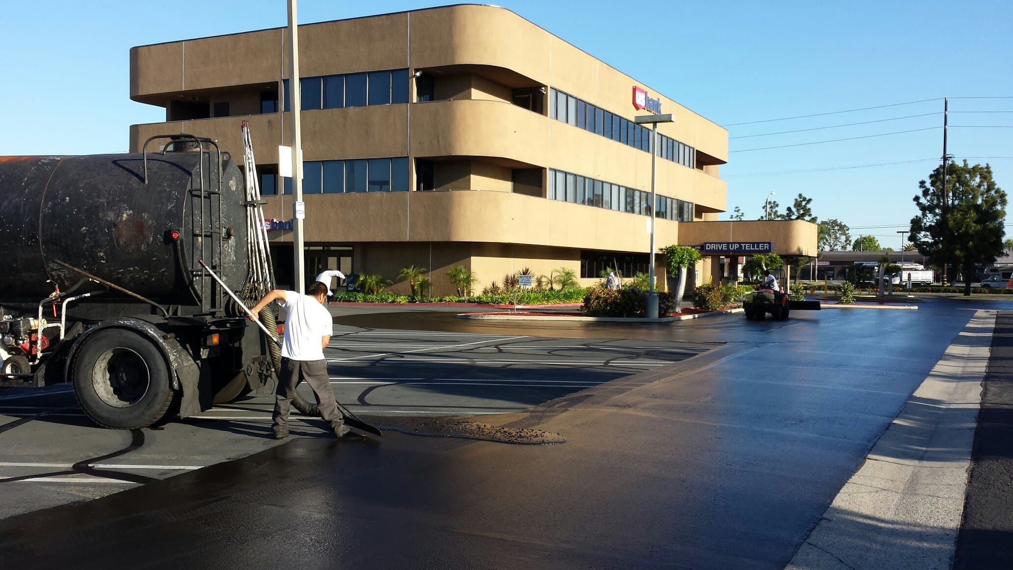 Seal coat tank truck and crew working in front of an office building